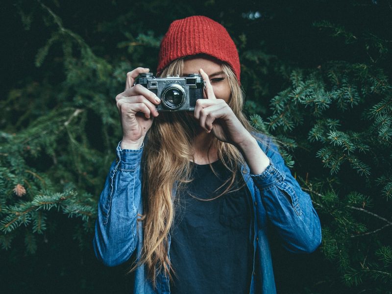 Woman in red beanie and blue jacket holding camera