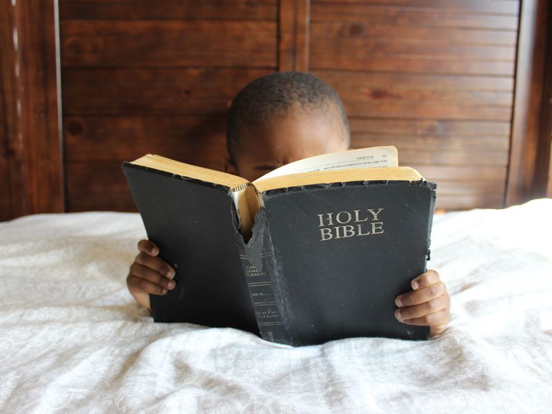 child reading bible on bed