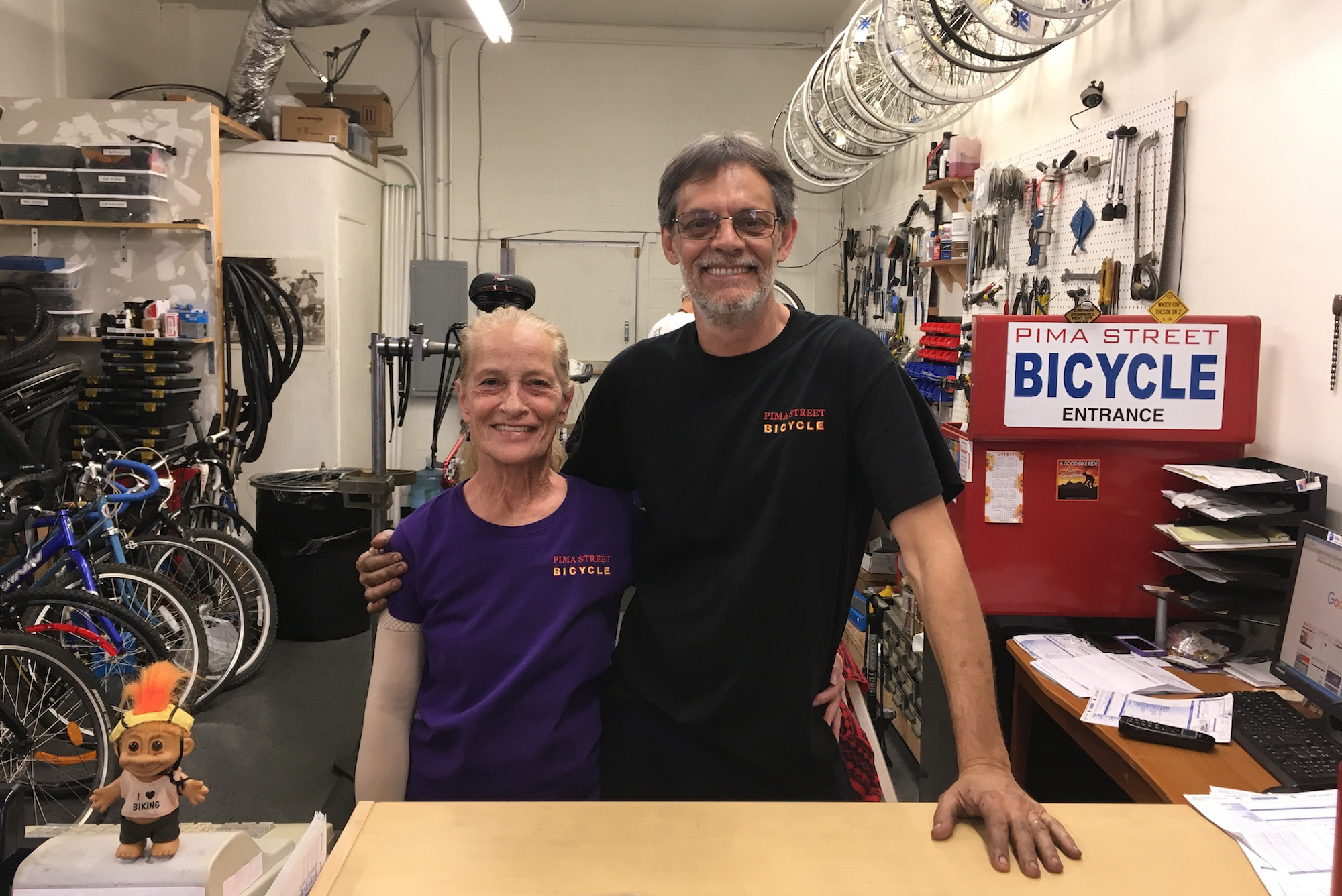 man and woman stand behind the counter of a bike shop smiling