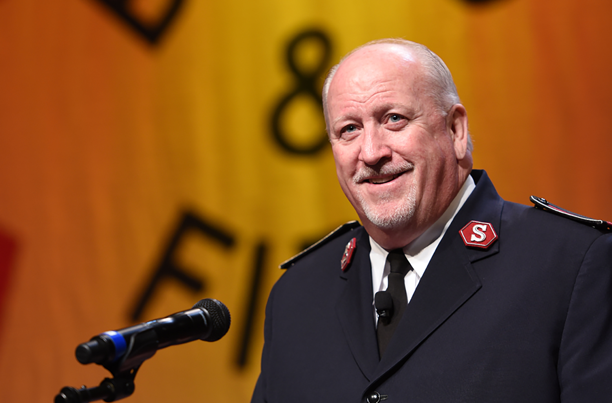 male salvation army officer speaks into a microphone on stage